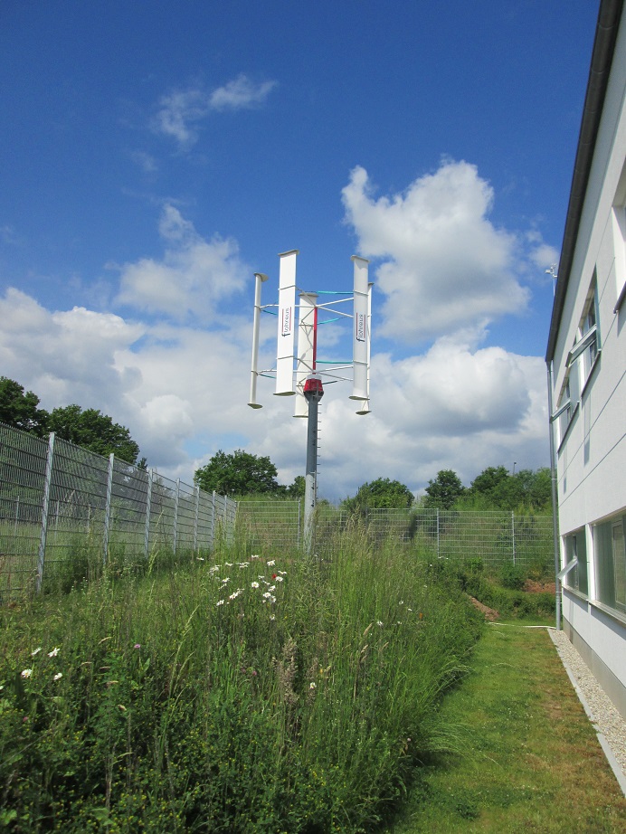 Wiese mit Kleinwindkraftanlage neben Gebäude